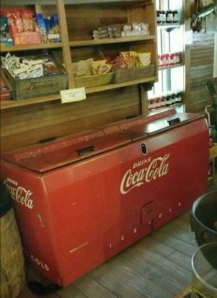Vintage Coca-Cola cooler in a nostalgic old store setting with wooden shelves and retro snack displays.