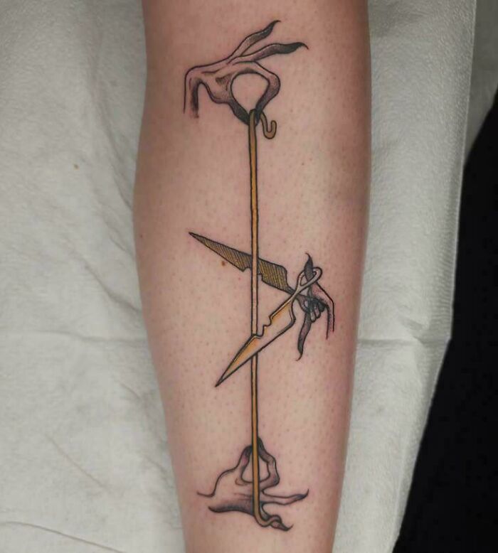 A stunning tattoo featuring abstract hands, a golden line, and sharp dagger-like forms on a person's leg.