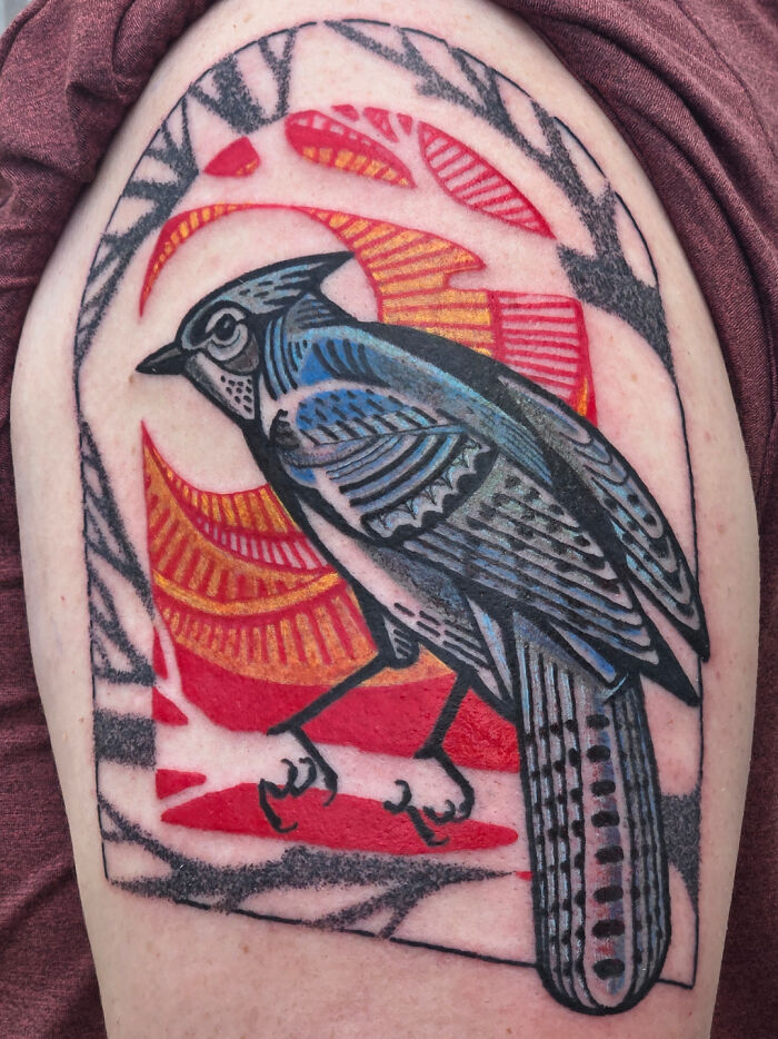 A vibrant, stunning tattoo of a blue jay bird on an arm, featuring intricate patterns and a red and gold background, illustrating stunning tattoos.