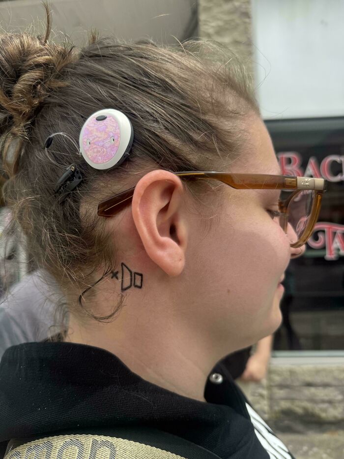 A person with a cochlear implant and a small neck tattoo behind their ear. The tattoo says DO. The stunning tattoos are permanent.