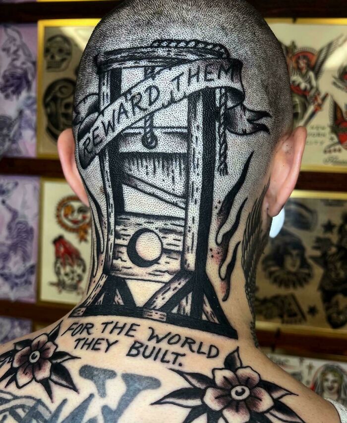 A stunning tattoo of a guillotine with text on the back of a person's head, surrounded by other stunning tattoos.