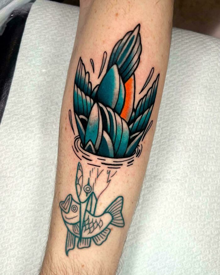 A vibrant, traditional style tattoo on an arm showing a duck diving into water, with a fish looking up from below.