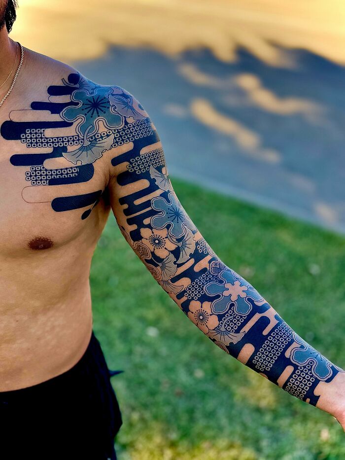 A man with a full arm and shoulder tattoo featuring a vibrant blue and white floral and geometric design. A stunning tattoo.