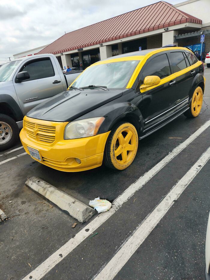 A black car with yellow DiWHY paint on the front bumper, grille, roofline, mirrors, and rims.