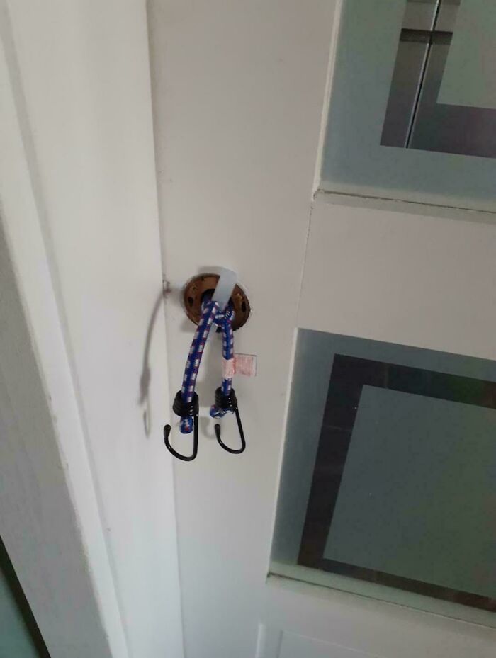 A white door with a bungee cord attached to a missing doorknob, showcasing a DiWHY attempt.