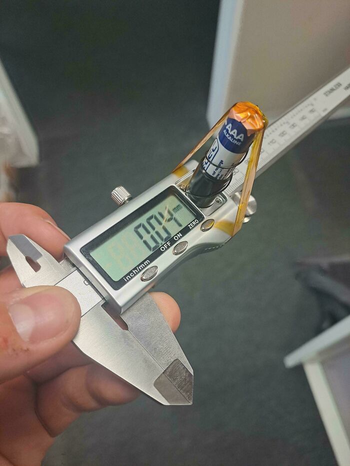 A hand holding digital calipers powered by a AAA battery in a DiWHY attempt. The display reads 0.04.