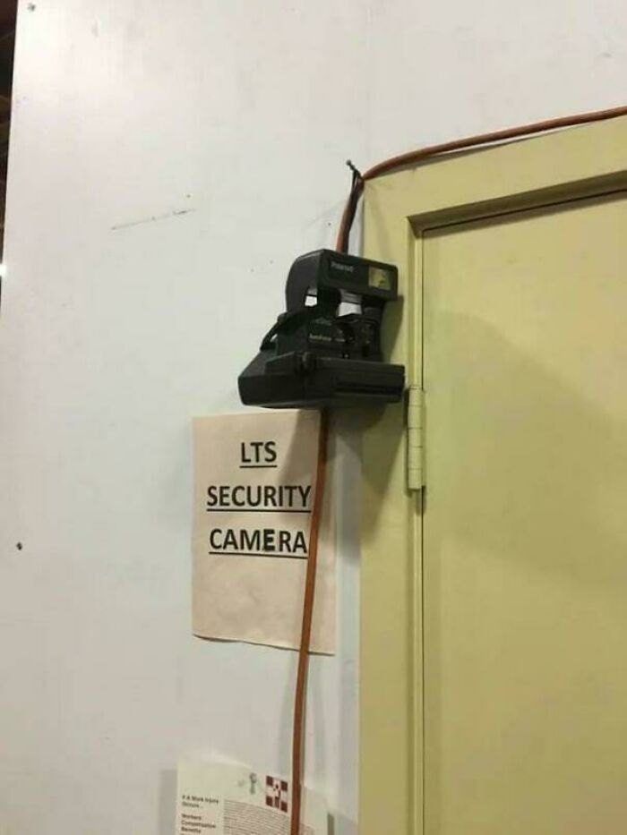 A funny DiWHY moment: a Polaroid camera labeled LTS Security Camera, haphazardly taped to a wall next to a door.