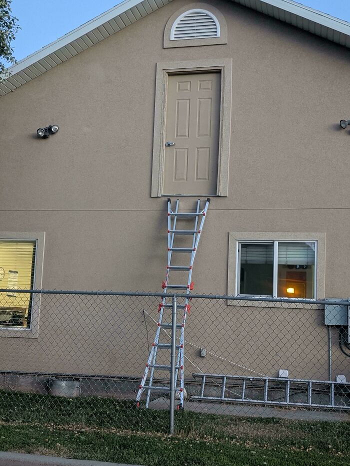 A ladder leans precariously against a house, leading to a door that opens to nowhere, a DiWHY fail.