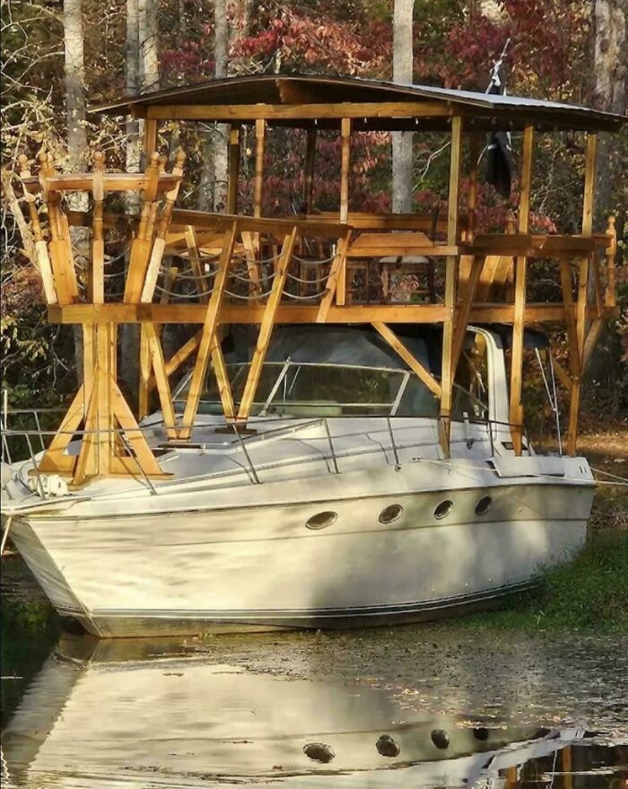 A boat with a wooden DiWHY structure built on top, parked in shallow water by the grass, showing a failed attempt.