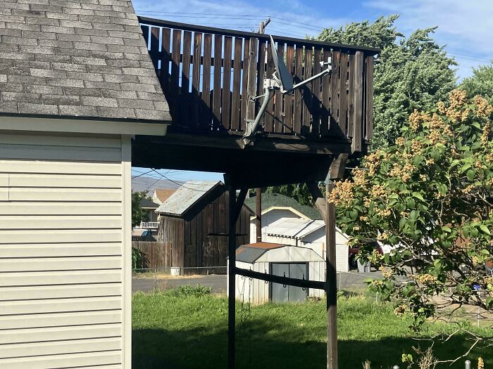 DiWHY satellite dish precariously mounted on a wooden deck, showing a DIY failure overlooking a yard.