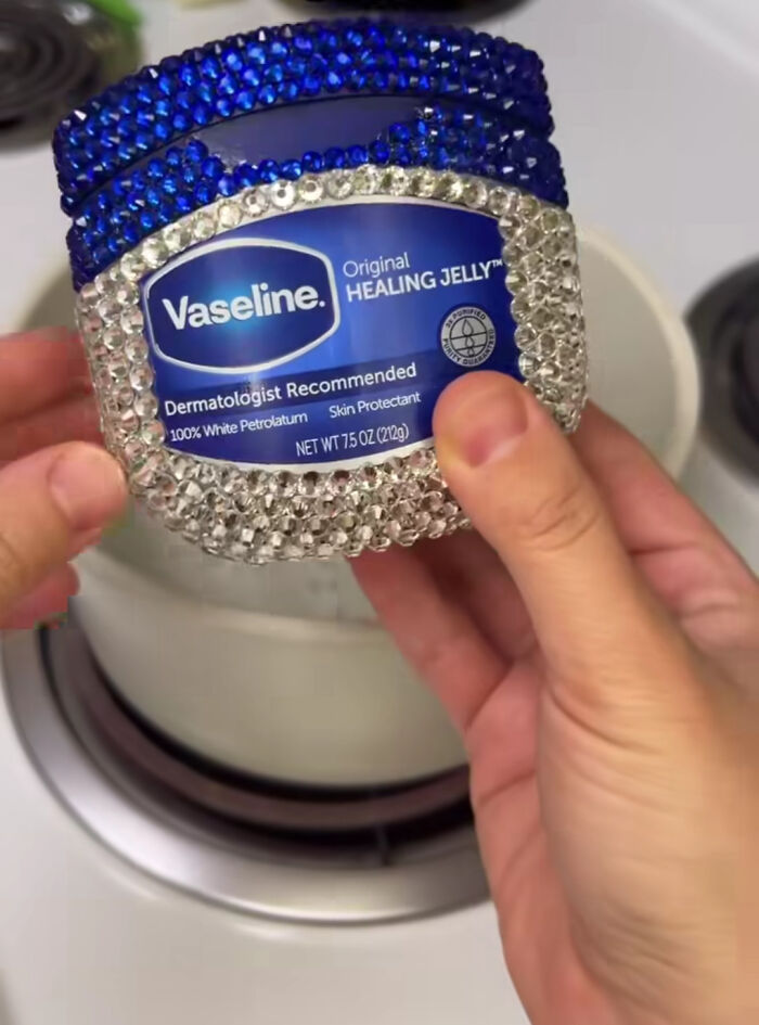 Hands holding a "DiWHY" bedazzled Vaseline jar over a pot. Blue and clear jewels adorn the jar.
