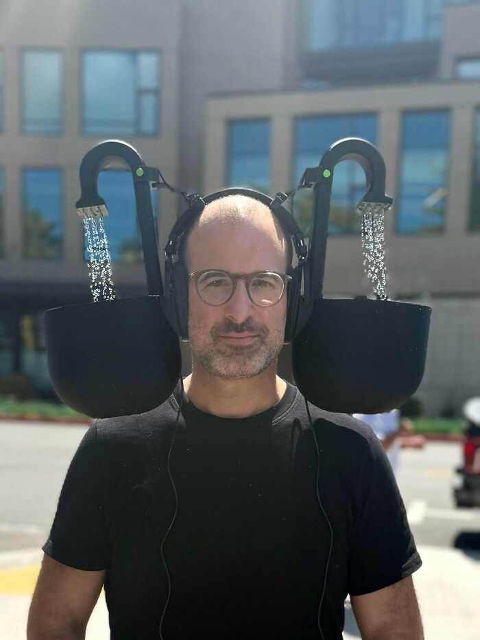 A man in glasses and headphones with showerheads and buckets over his ears, a perfect example of DiWHY.