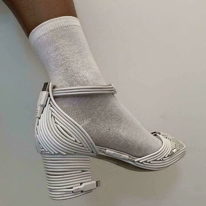 A foot in a white sock wearing a high-heeled shoe made from woven white charging cables. A clear DiWHY example.