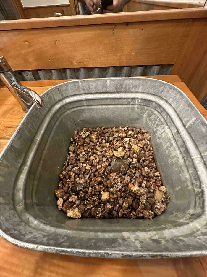 A DiWHY example: a metal basin filled with rocks serves as a sink, next to a silver faucet.