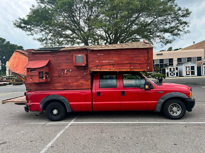 A red pickup truck with a large, homemade wooden camper on the back. A DiWHY example of a DIY RV.