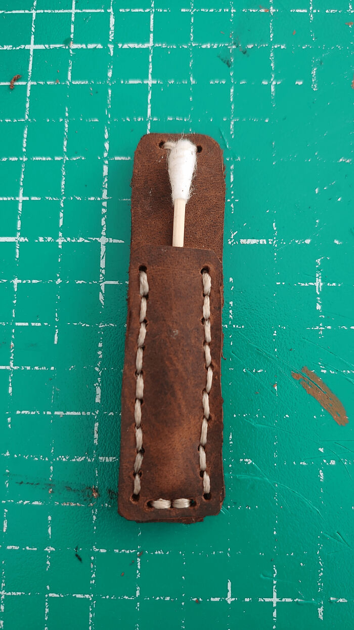 Close-up of a brown leather holder with white stitching, containing a cotton swab. A DiWHY project in progress.