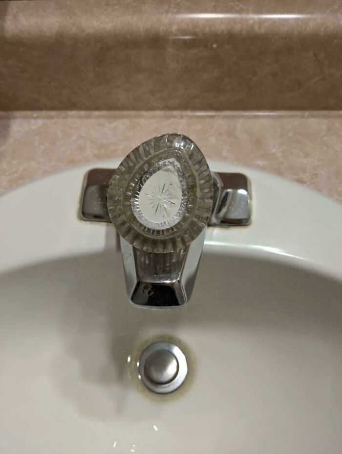A close-up view of a clear plastic faucet handle with a starburst design, a nostalgic 90s bathroom fixture.
