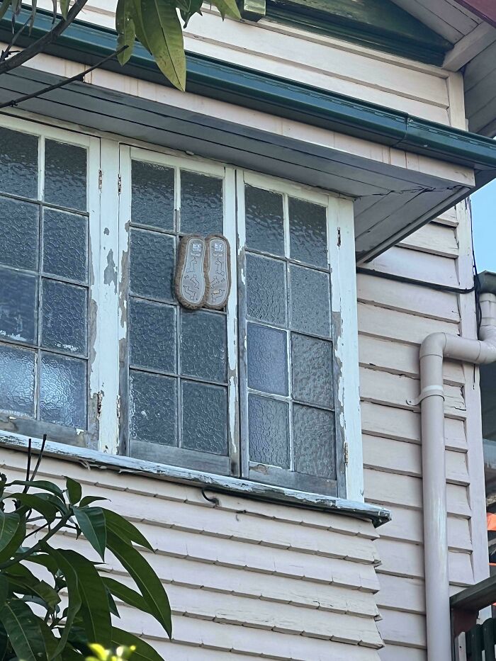 Old window on a house with worn paint and sandals nailed to the closed panes as a dumb but technically works solution.