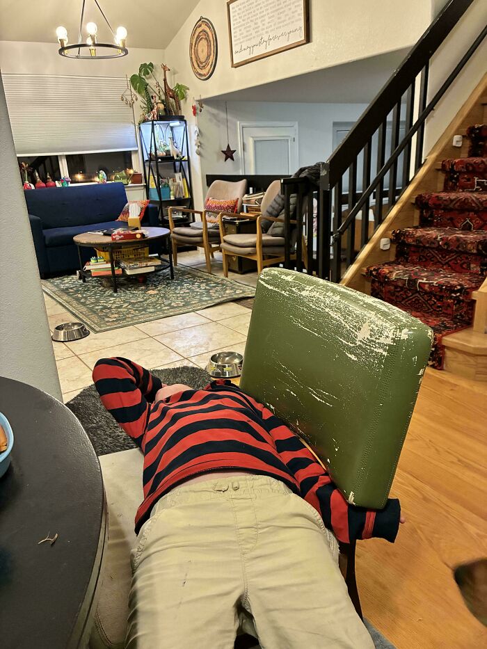 A child in a red and black striped shirt rests against a green chair. Focuses on dads and family life.