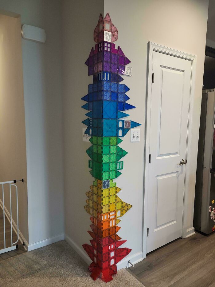A tall, colorful structure made of magnetic tiles stands in a corner, showcasing creativity from an online community for dads.