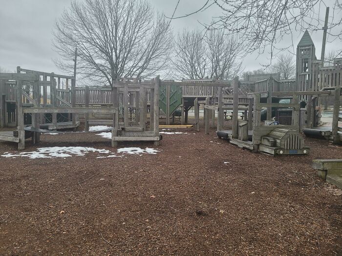 A vast wooden playground with various structures and a truck-shaped play area on a mulch ground, with patches of snow. Dedicated to Dads.