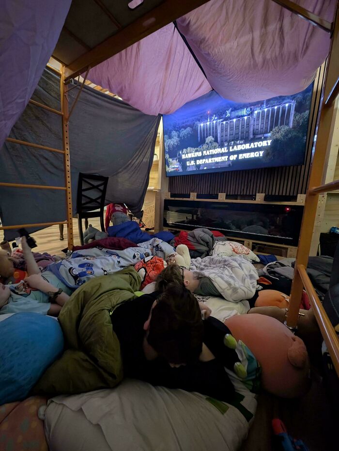 Children asleep under blankets in a blanket fort watching a movie, a feel-good image for dads.