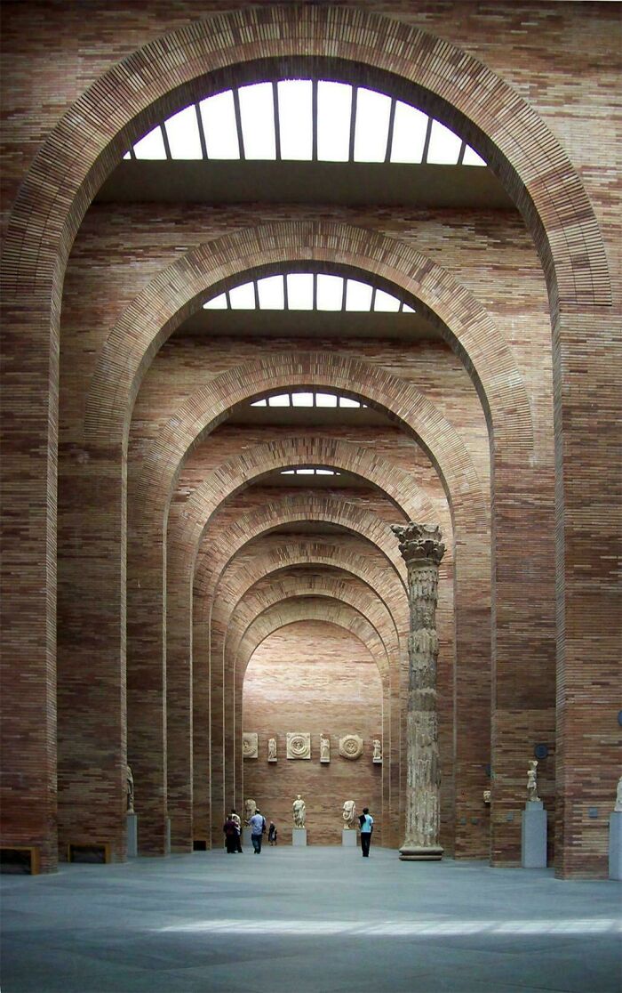 Grand hall with a series of brick arches, skylights, and ancient-style sculptures, showcasing impressive architecture.