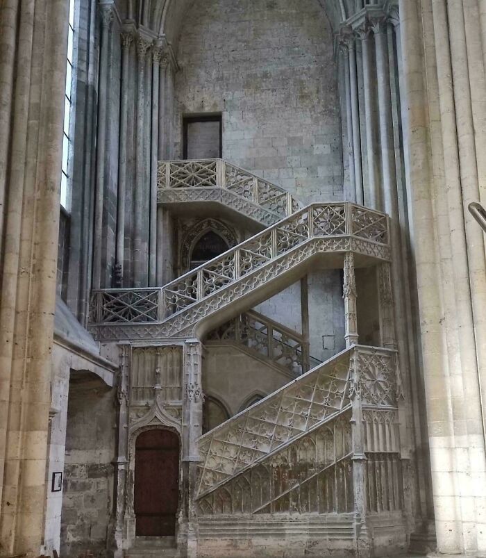 Impressive multi-tiered gothic stone staircase with ornate railings, within a large historical building. Architecture lovers will appreciate this.