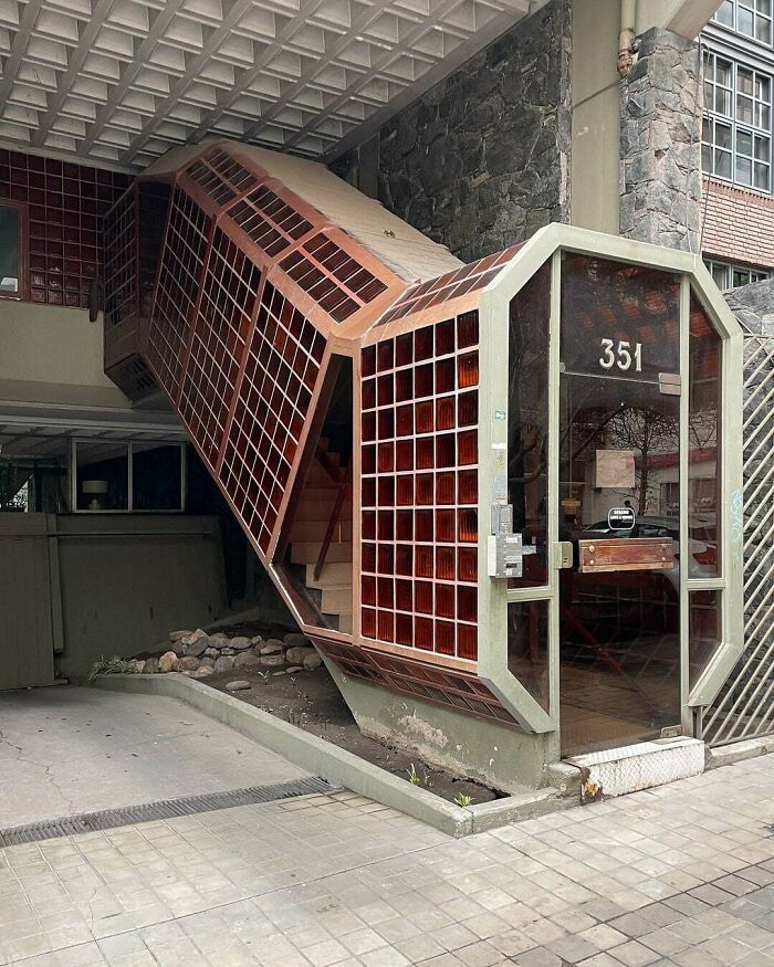 An unusual, angled stairwell with red grid-patterned windows leads to a building entrance labeled 351, impressing architecture lovers.