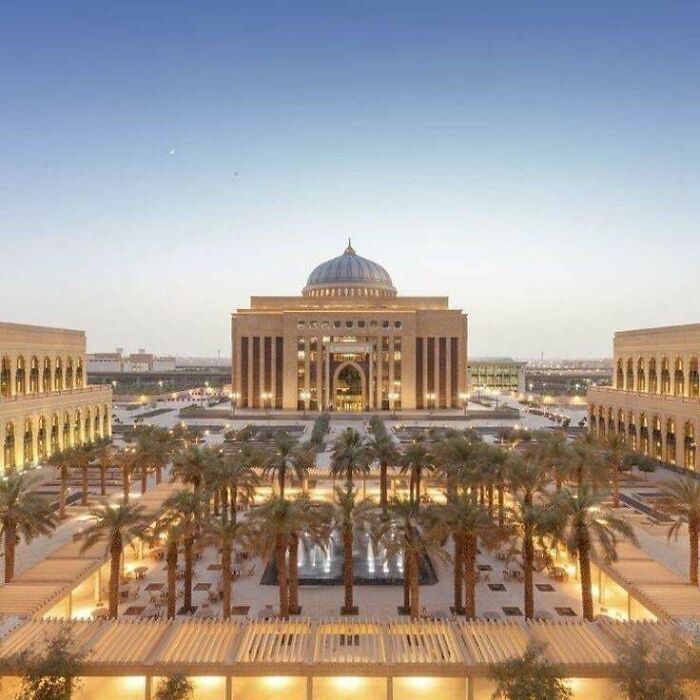 Majestic building with a dome, illuminated at dusk, surrounded by palm trees and fountains. Impressive architecture.