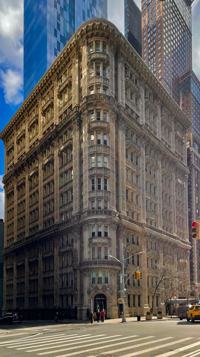 A detailed, ornate building with a rounded corner, showcasing impressive architecture in an urban setting under a cloudy sky.