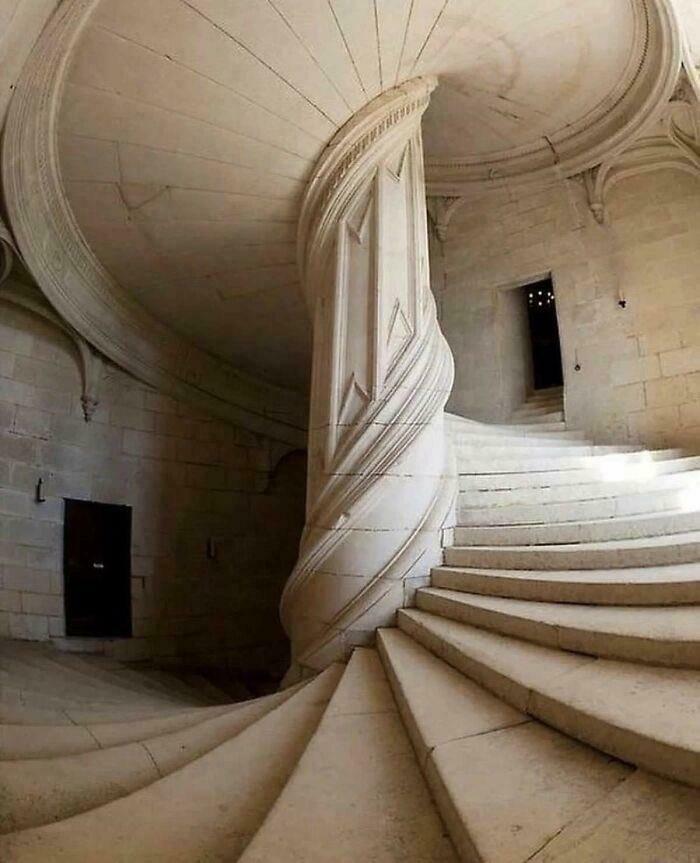 Impressive architecture: a grand spiral staircase made of white stone, winding upwards with a central ornate column.