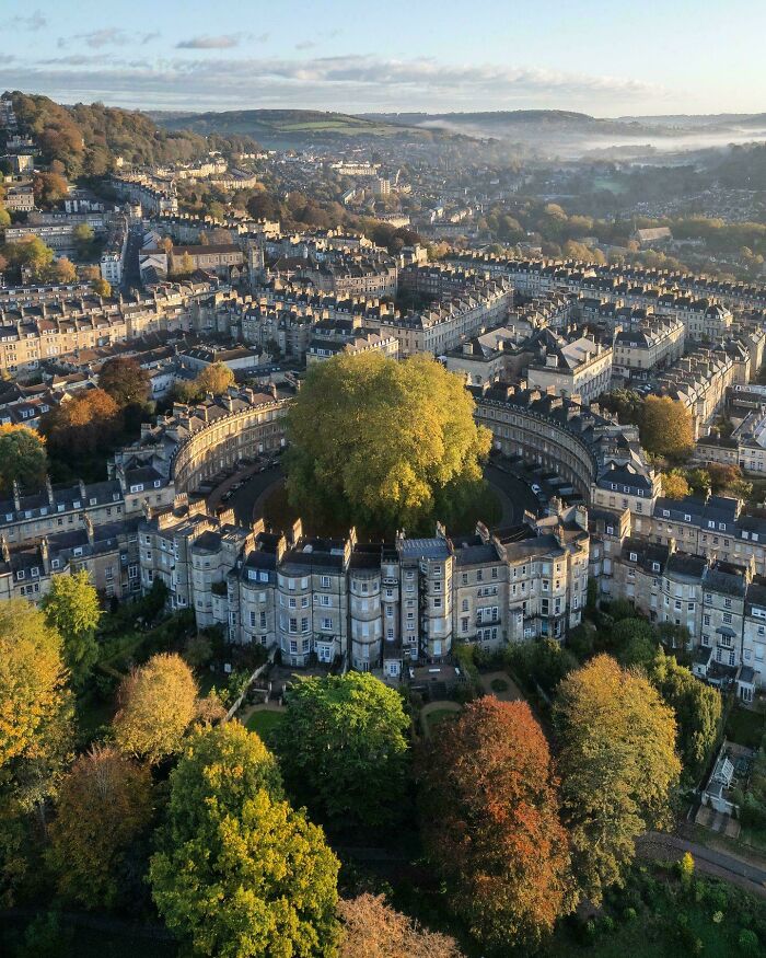 Aerial view of the Royal Crescent in Bath, a stunning example of impressive building architecture, surrounded by autumn trees.