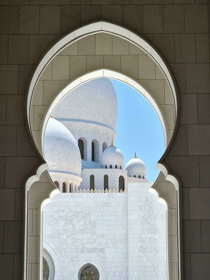 A breathtaking view of a grand mosque through an elegant arched window, showcasing impressive architecture.