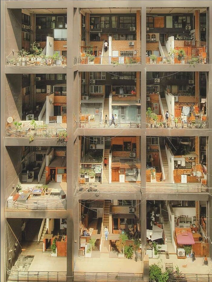 A multi-story building, sectioned into open-air living spaces with balconies, stairs, and people. Impressive architecture.