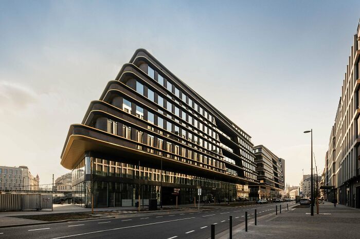 An impressive modern building with curved, dark layered facades and reflective windows, seen from a street, showcasing stunning architecture.