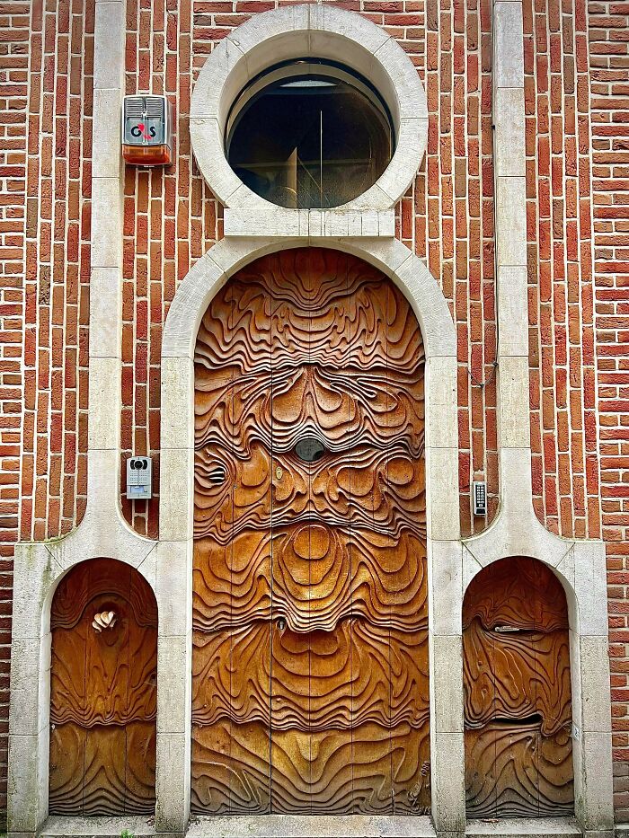 An impressive building with a red brick facade, intricate carved wooden doors with wave-like patterns, and a round window. Architecture lovers will appreciate the unique design.