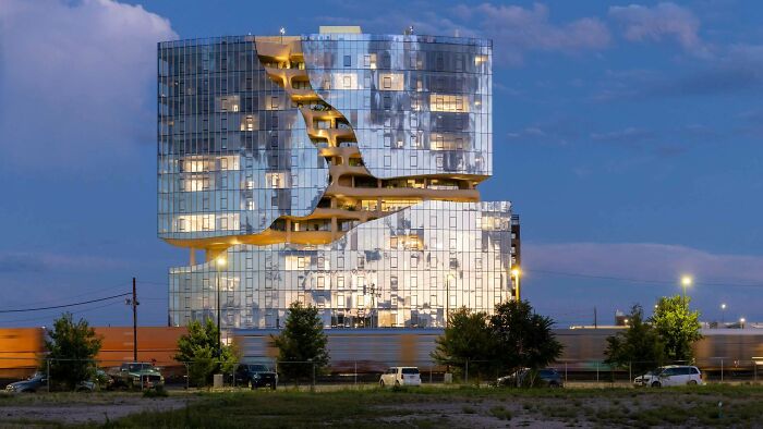 Modern glass architecture building with a wavy cut-out, illuminated at dusk, showcasing impressive architecture.