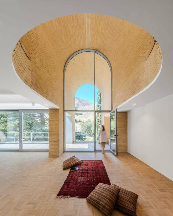 Stunning architecture featuring a high arched window looking out to mountains, with a person walking towards the exit.