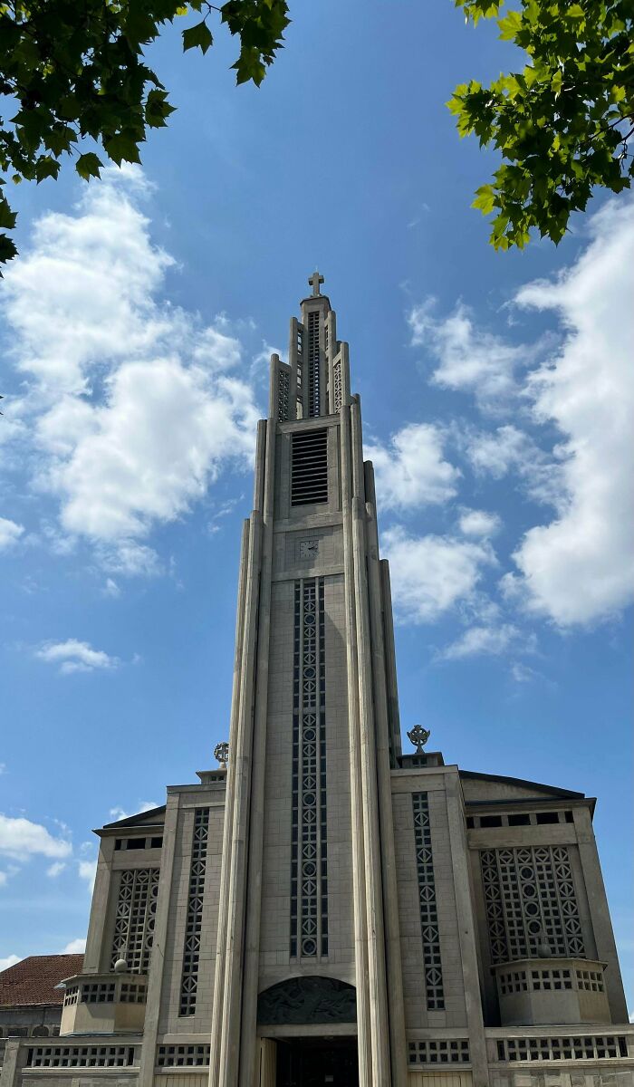 An upward view of a tall, grey church tower under a blue sky with white clouds, showcasing impressive building architecture.