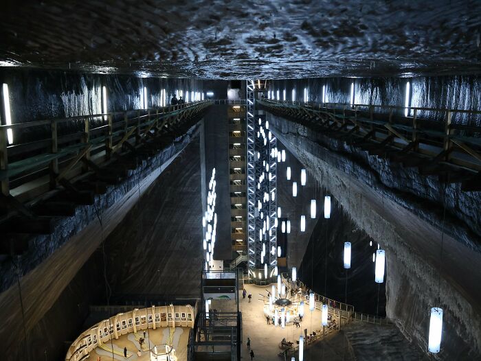 A vast underground space with illuminated walkways, a central lit area, and modern suspended lights. Impressive architecture.