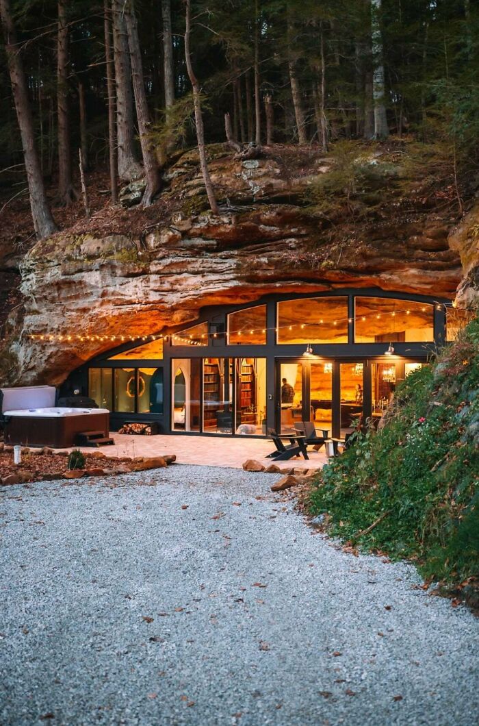 An impressive building: a modern home built into a rocky cliff with large windows, a hot tub, and outdoor seating. Architecture lovers will appreciate this unique design.