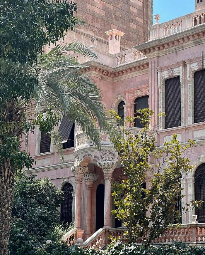 An impressive pink building with intricate architecture, a curved balcony, and palm trees, showcasing a beautiful building.