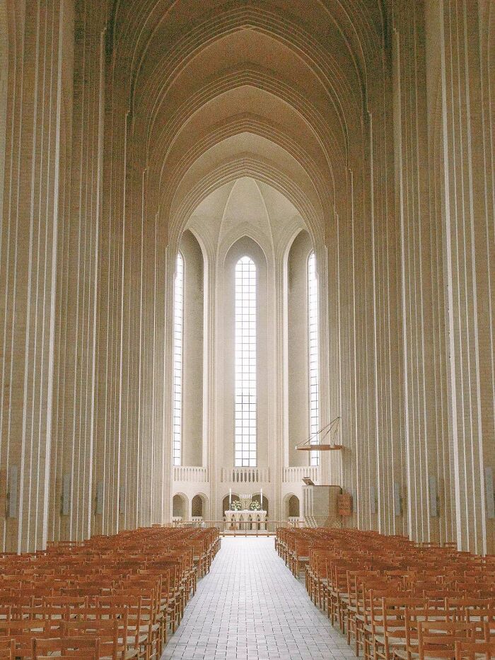 An impressive interior of a modern church with towering arches, tall windows, and rows of wooden chairs, showcasing stunning building architecture.