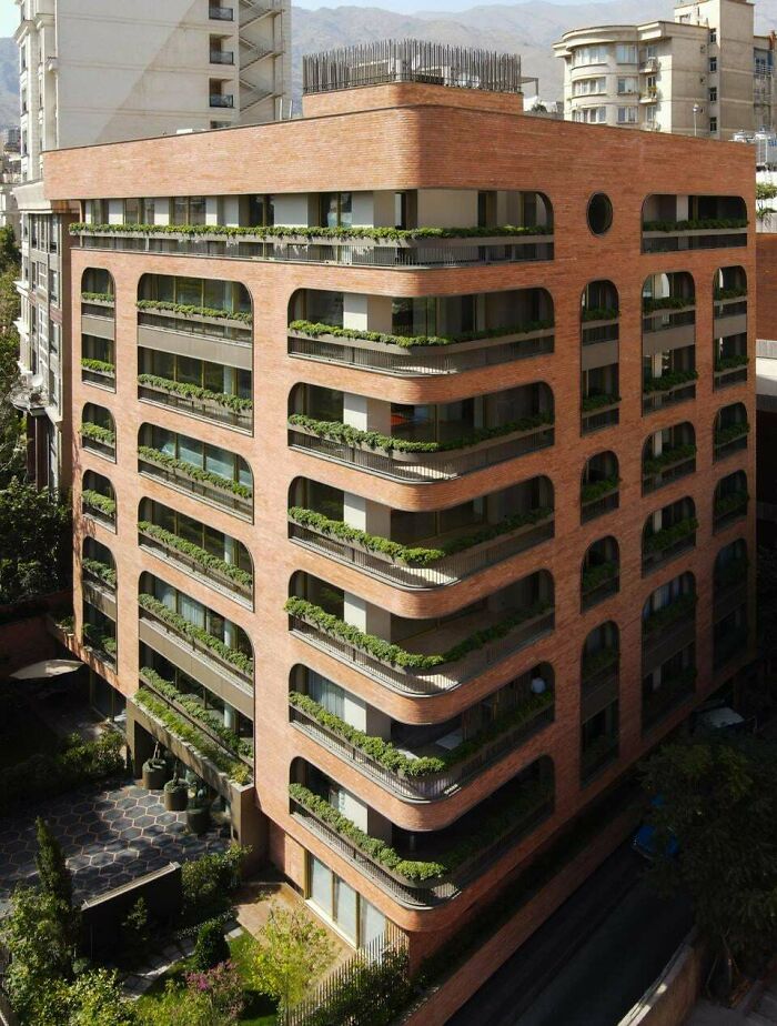 Impressive architecture with a brick facade and rounded arches, featuring balconies with lush green plants.