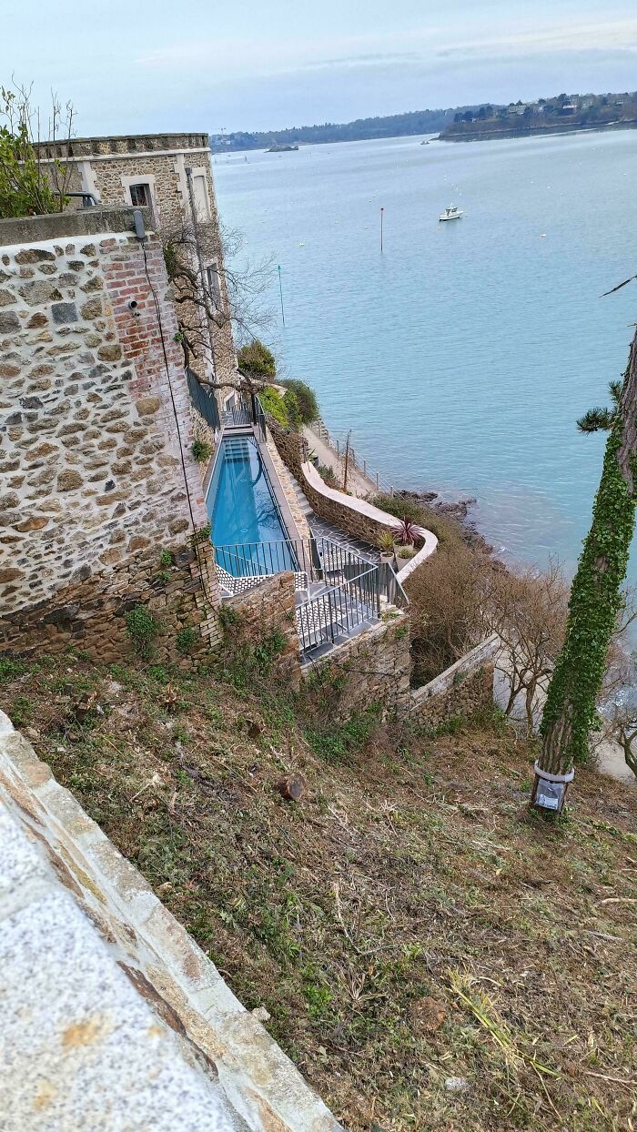 Impressive architecture: a narrow pool built into a stone cliffside home, overlooking a blue body of water with a boat.