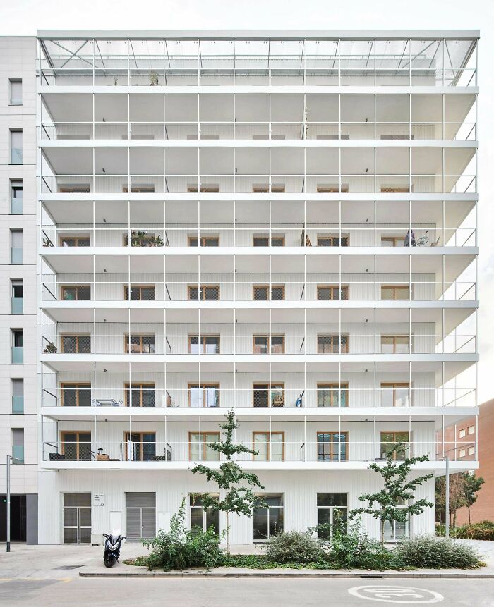An impressive modern white building with multiple balconies and a transparent upper facade, showcasing stunning architecture.