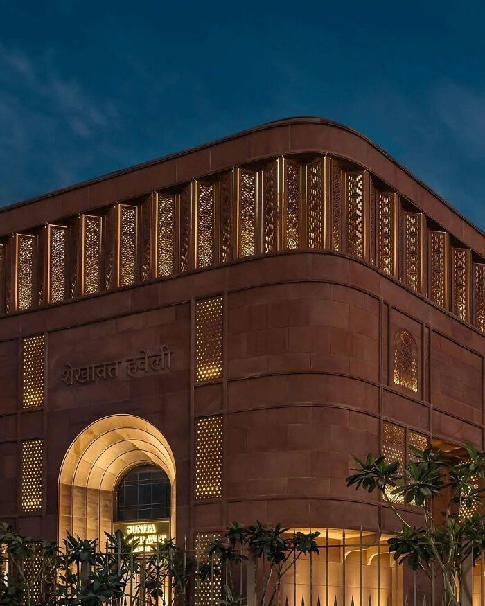A beautiful, illuminated brown architecture building at dusk, featuring intricate lattice work and an impressive archway.