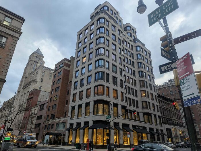 Street view of a curved, modern building in a city, with cars and street signs visible. Impressive architecture.