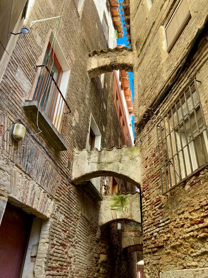 Narrow alley with old brick buildings connected by arched bridges, showcasing impressive architecture in an intriguing way.
